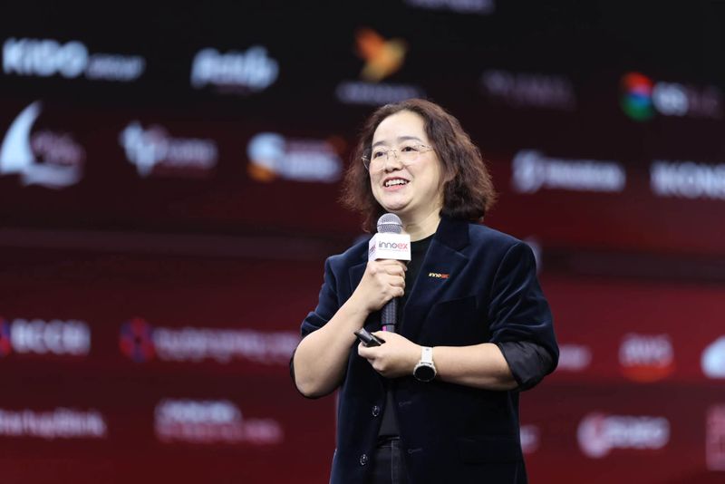Bà Nguyễn Thị Diệu Hằng cầm micro phát biểu trên sân khấu InnoEx, phía sau là tường logo đối tác