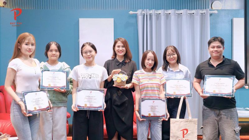Học viên khoá Luyện giọng ứng dụng cầm giấy hoàn thành khoá trong phòng học có logo Đạt Phi