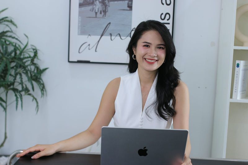 Vũ Hà Trang mỉm cười ngồi bên bàn làm việc với máy tính