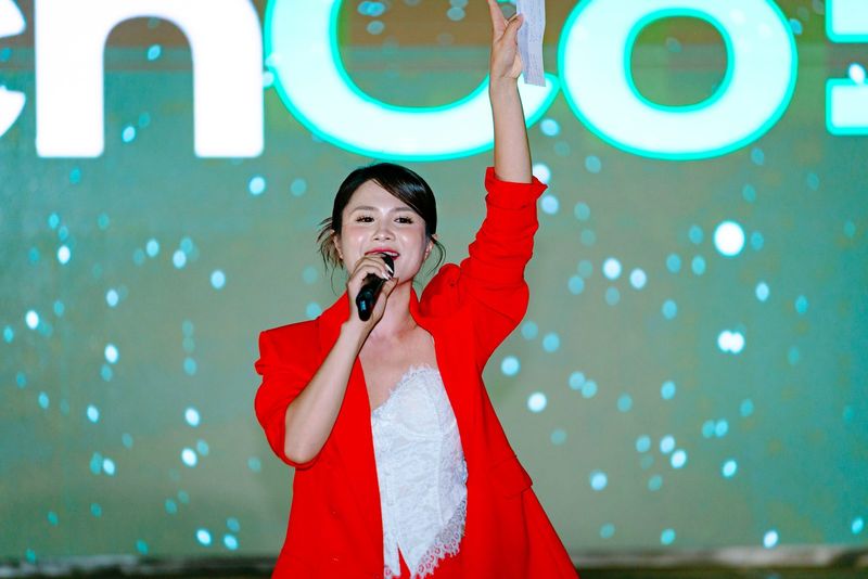 Vũ Hà Trang áo khoác đỏ cầm micro và giơ cao tờ giấy trước màn LED TechCore
